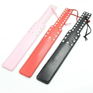 A striking BDSM slave beater spanking paddle with metal studs and a knotted cord handle in black, pink, and red variants.